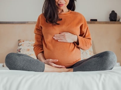 a female orthodontic patient sitting on the bed holding her belly because she is pregnant