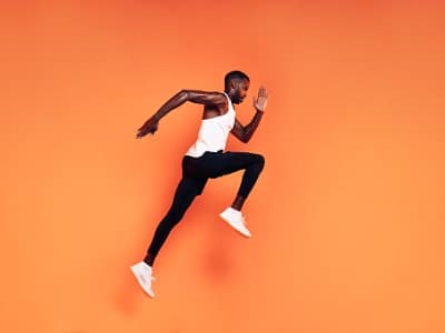 an athletic man running in front of a orange background