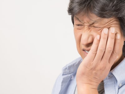 an orthodontic patient holding their cheek because of braces pain and canker sores