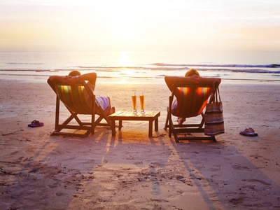 a couple with braces sitting on beach chairs facing the beach with two drinks in between them