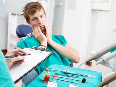 A man sitting in a dentist's chair while massaging his gums.