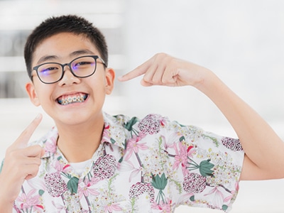 Teen receiving early orthodontic treatment with blue braces pointing to his braces