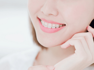 A woman with braces smiling with her hand on her chin.