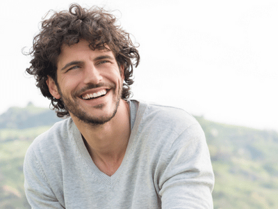 A man with curly hair is smiling with his teeth supported by an orthodontic expander.
