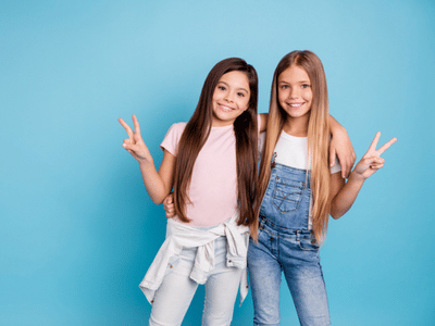 Two young girls with braces posing for a photo on a blue background.