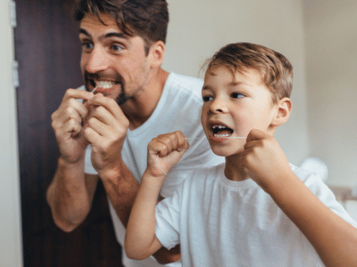 A father and son flossing their teeth in the bathroom.
