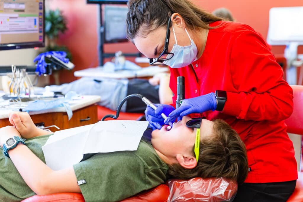 A woman is examining a boy's teeth in an orthodontics office.