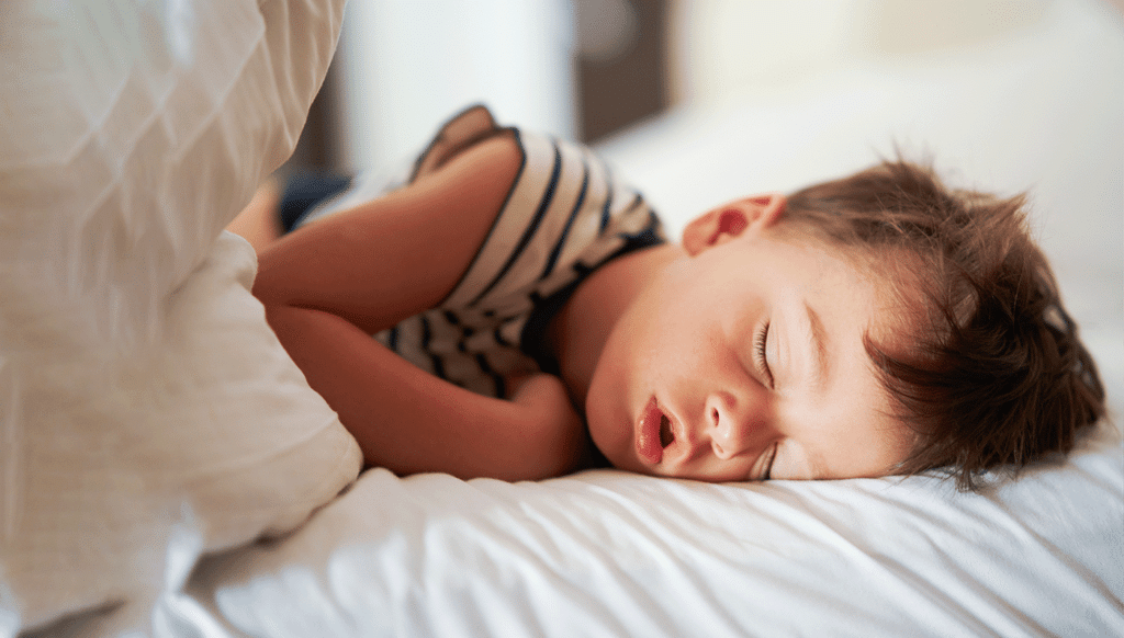 A child sleeps on a white bed with their mouth open